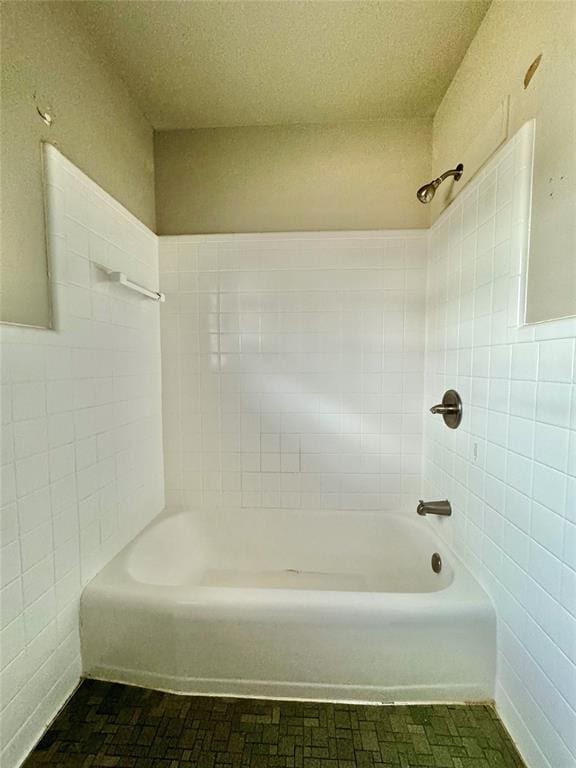 bathroom featuring a textured ceiling, tiled shower / bath combo, and tile walls