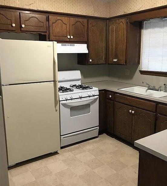 kitchen with dark brown cabinets, sink, exhaust hood, and white appliances