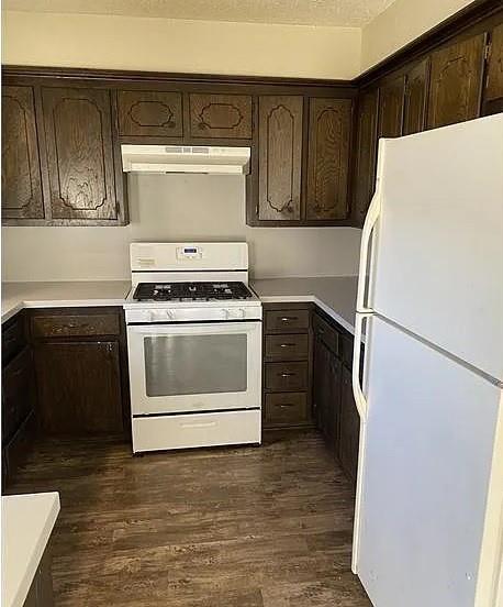 9816 NE 5th St, Midwest City, OK 73130 - kitchen featuring white appliances, under cabinet range hood, dark brown cabinets, dark wood-style flooring, and light countertops