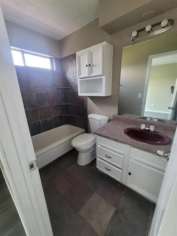 full bathroom with vanity, tile patterned floors, tiled shower / bath, toilet, and a textured ceiling