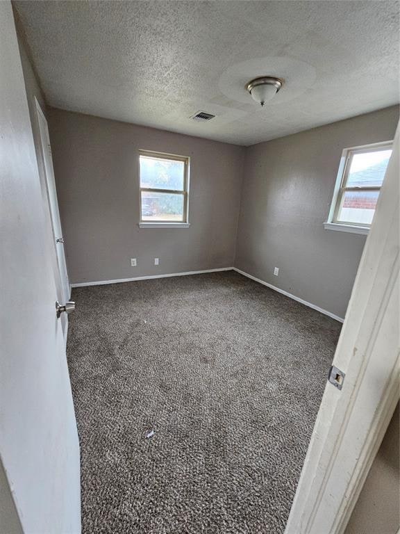 empty room with a textured ceiling, dark carpet, and plenty of natural light