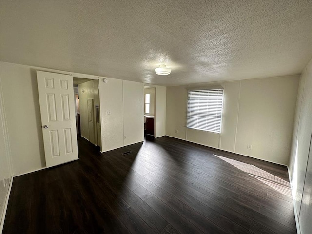 empty room with dark hardwood / wood-style floors and a textured ceiling