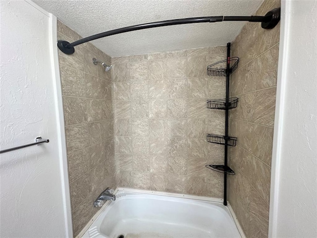 bathroom with a textured ceiling and tiled shower / bath