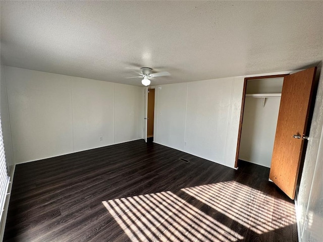 unfurnished bedroom with ceiling fan, a closet, dark wood-type flooring, and a textured ceiling