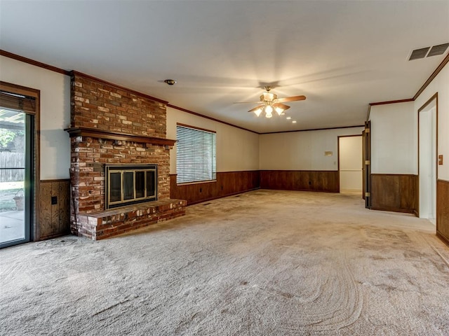 unfurnished living room with ceiling fan, light carpet, crown molding, wooden walls, and a fireplace