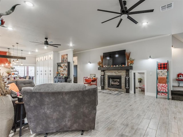 living room with ceiling fan, a stone fireplace, light wood-type flooring, and crown molding