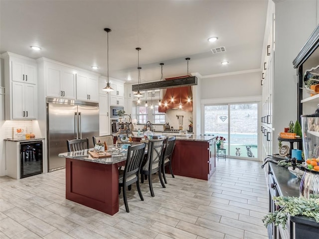 kitchen with a breakfast bar, light stone countertops, stainless steel built in fridge, and beverage cooler