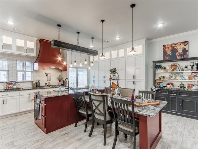 kitchen featuring light stone countertops, an island with sink, pendant lighting, a breakfast bar, and white cabinets