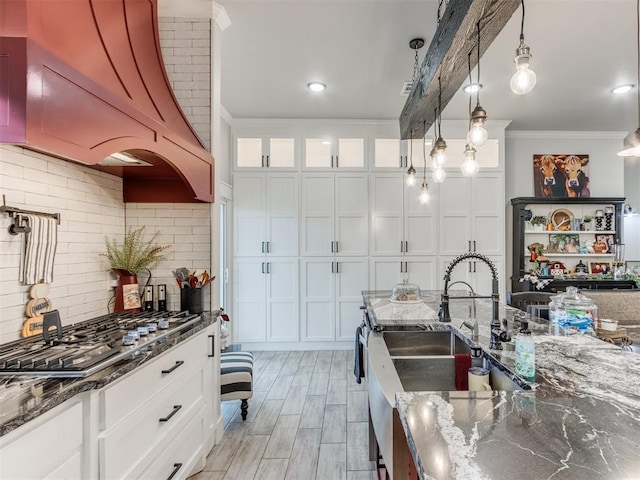 kitchen with premium range hood, pendant lighting, stainless steel gas stovetop, decorative backsplash, and white cabinets