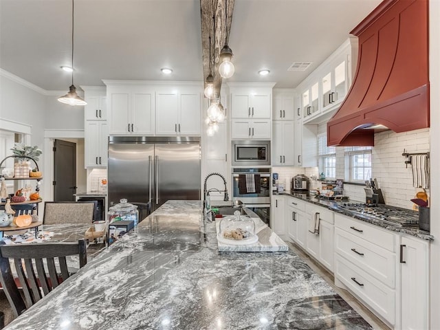 kitchen featuring built in appliances, white cabinetry, custom range hood, and decorative backsplash