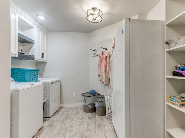 clothes washing area with cabinets, light wood-type flooring, and washing machine and dryer