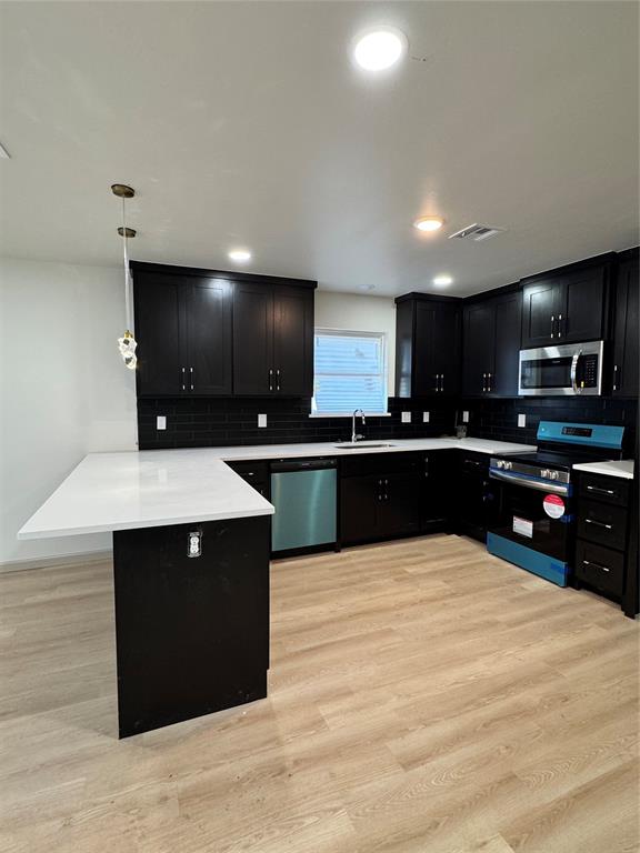 kitchen featuring kitchen peninsula, appliances with stainless steel finishes, tasteful backsplash, pendant lighting, and light hardwood / wood-style floors