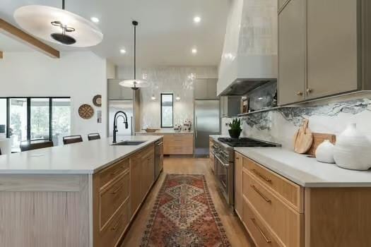 kitchen with hanging light fixtures, stainless steel appliances, sink, and a large island with sink