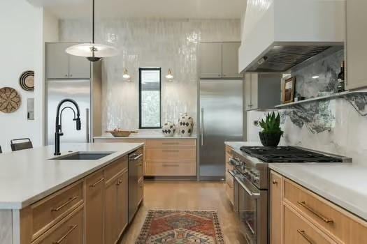 kitchen with sink, premium appliances, hanging light fixtures, a kitchen island with sink, and wall chimney range hood