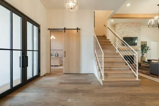 stairs featuring wood-type flooring, a barn door, a chandelier, and french doors