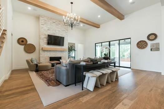 living room with a notable chandelier, beam ceiling, a fireplace, and light hardwood / wood-style floors