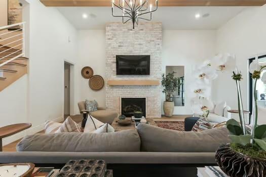 living room featuring an inviting chandelier, a brick fireplace, and beam ceiling