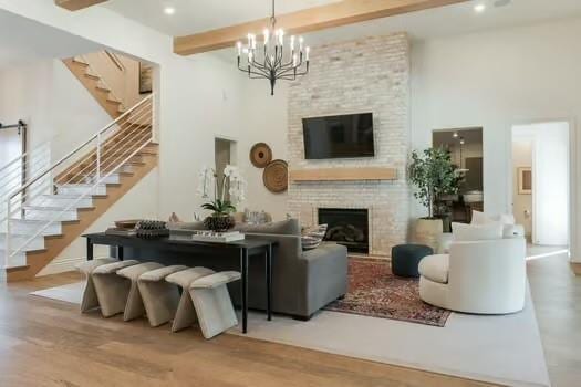 living room featuring beamed ceiling, wood-type flooring, a large fireplace, and a chandelier