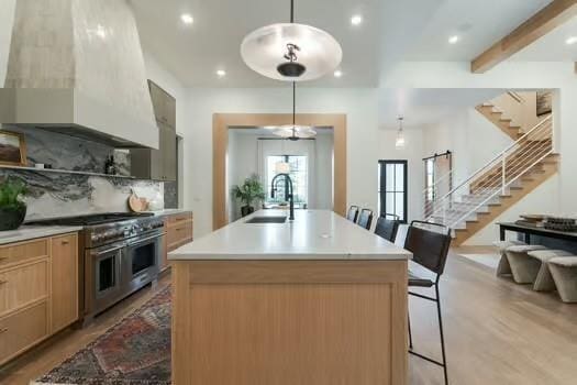 kitchen featuring double oven range, a breakfast bar area, wall chimney range hood, and an island with sink