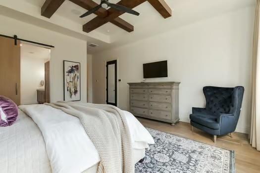 bedroom featuring beamed ceiling, coffered ceiling, ceiling fan, light hardwood / wood-style floors, and a barn door