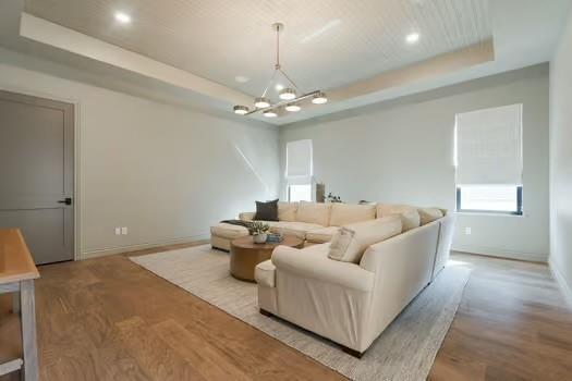 living room with a wealth of natural light, light hardwood / wood-style flooring, an inviting chandelier, and a tray ceiling