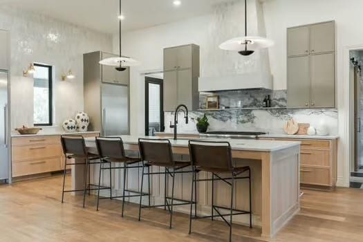 kitchen featuring sink, a breakfast bar area, a kitchen island with sink, hanging light fixtures, and tasteful backsplash