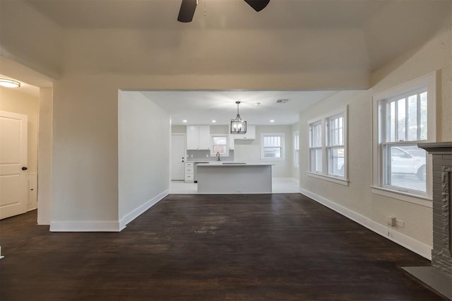 unfurnished living room with ceiling fan with notable chandelier, a brick fireplace, plenty of natural light, and dark wood-type flooring