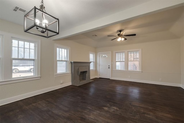 unfurnished living room featuring a wealth of natural light, ceiling fan with notable chandelier, and dark hardwood / wood-style floors