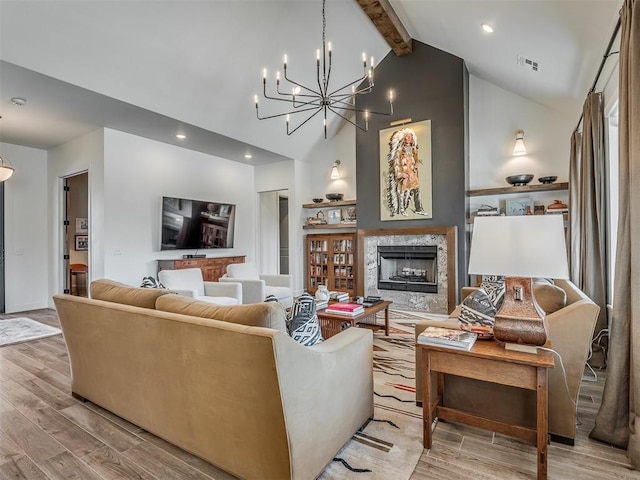 living room featuring a fireplace, beam ceiling, light hardwood / wood-style floors, and an inviting chandelier