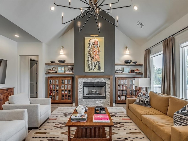 living room featuring a premium fireplace, light hardwood / wood-style flooring, high vaulted ceiling, and a chandelier