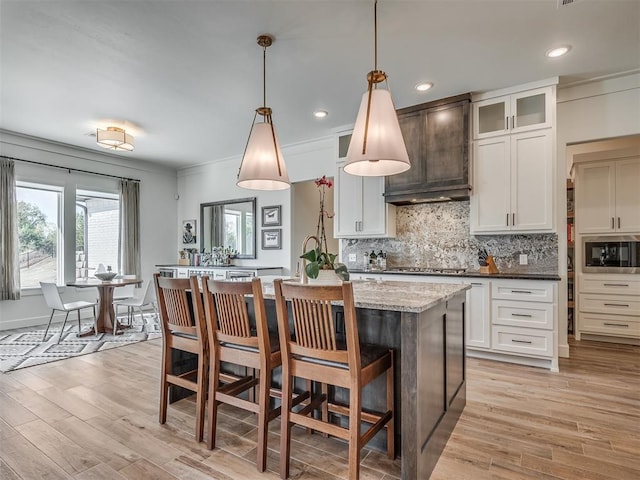 kitchen featuring pendant lighting, a kitchen island with sink, white cabinets, light hardwood / wood-style floors, and light stone counters