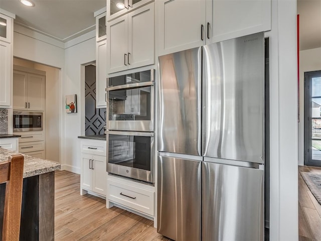 kitchen featuring dark stone countertops, white cabinets, light wood-type flooring, and appliances with stainless steel finishes