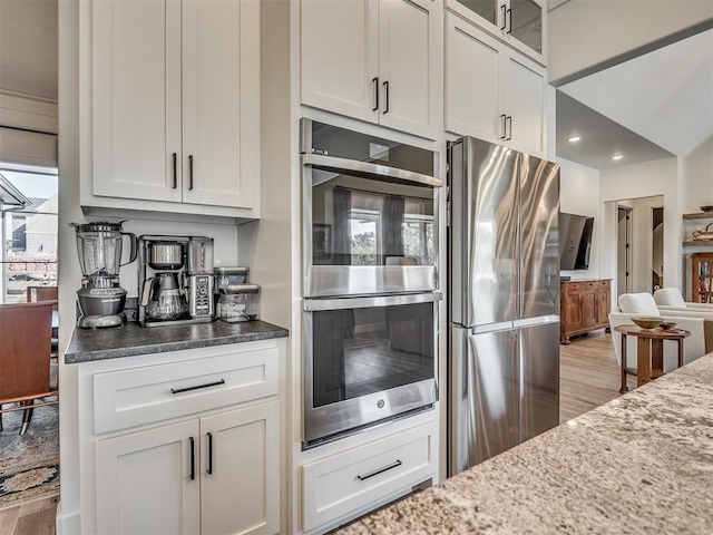 kitchen featuring light wood-type flooring, stainless steel appliances, white cabinetry, and dark stone counters