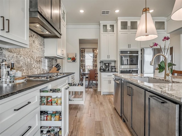 kitchen with appliances with stainless steel finishes, light wood-type flooring, sink, pendant lighting, and white cabinets