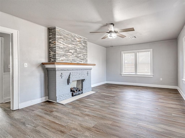 unfurnished living room with a fireplace, wood-type flooring, a textured ceiling, and ceiling fan