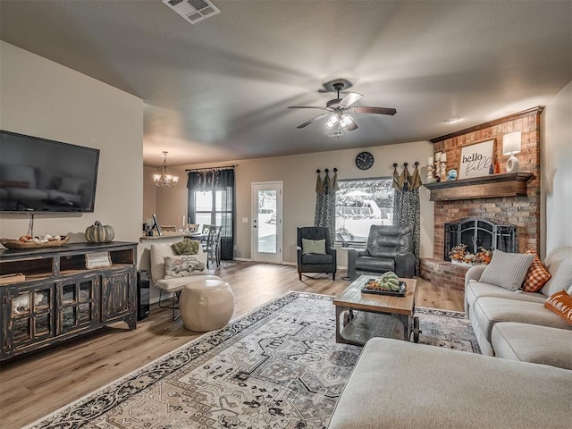 living room featuring a brick fireplace, ceiling fan with notable chandelier, and light hardwood / wood-style flooring