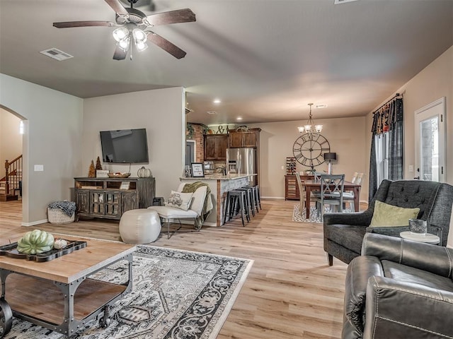 living room featuring ceiling fan with notable chandelier and light hardwood / wood-style flooring