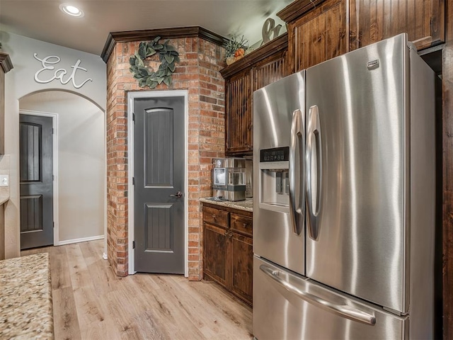 kitchen featuring dark brown cabinetry, light stone counters, stainless steel refrigerator with ice dispenser, and light wood-type flooring