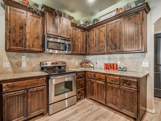 kitchen with light stone counters, appliances with stainless steel finishes, and light hardwood / wood-style flooring