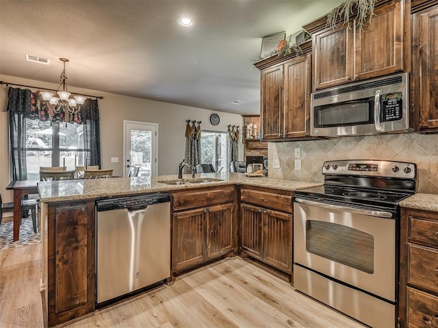 kitchen with sink, light hardwood / wood-style flooring, a notable chandelier, kitchen peninsula, and stainless steel appliances