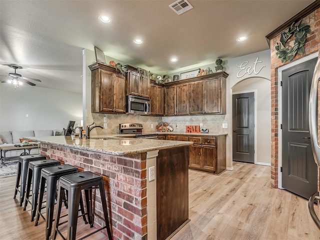 kitchen with kitchen peninsula, appliances with stainless steel finishes, light wood-type flooring, light stone countertops, and ceiling fan