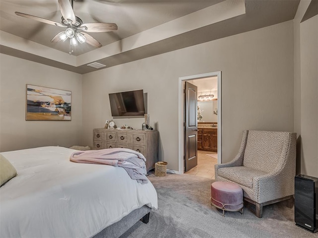 bedroom with ensuite bath, a raised ceiling, ceiling fan, and light colored carpet