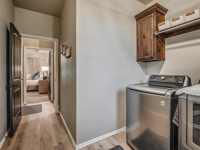 clothes washing area featuring cabinets, light wood-type flooring, and washer / clothes dryer