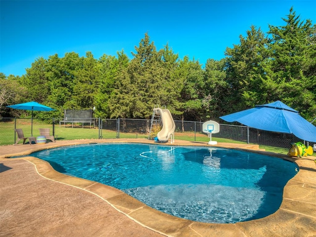 view of swimming pool featuring a yard, a water slide, and a trampoline