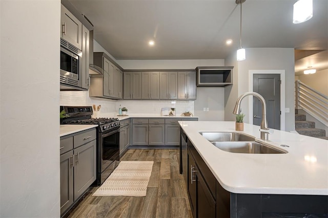 kitchen with stainless steel microwave, gas stove, a kitchen island with sink, hanging light fixtures, and sink