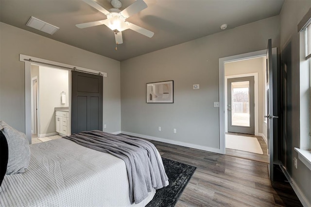 bedroom with dark wood-type flooring, ceiling fan, connected bathroom, and a barn door