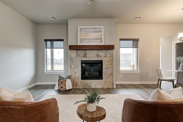 living room featuring a tiled fireplace, plenty of natural light, and wood-type flooring