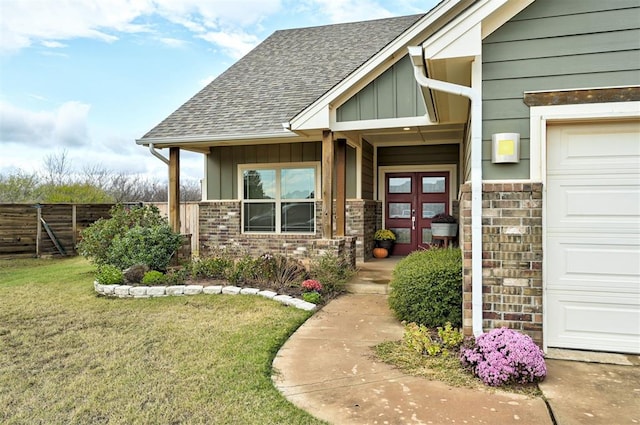 view of exterior entry with brick siding, a lawn, an attached garage, board and batten siding, and fence