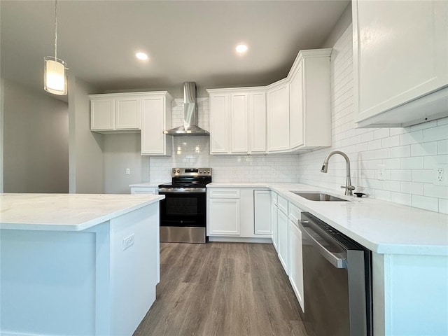 kitchen with white cabinets, hanging light fixtures, wall chimney exhaust hood, appliances with stainless steel finishes, and wood-type flooring