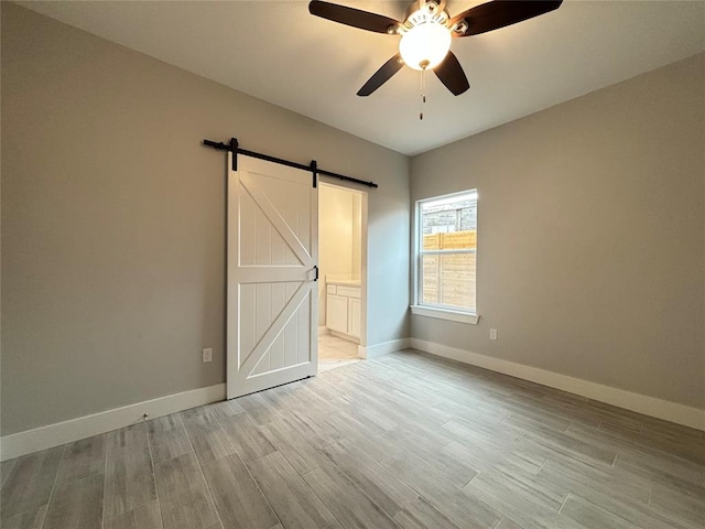 unfurnished bedroom featuring connected bathroom, a barn door, ceiling fan, and light wood-type flooring